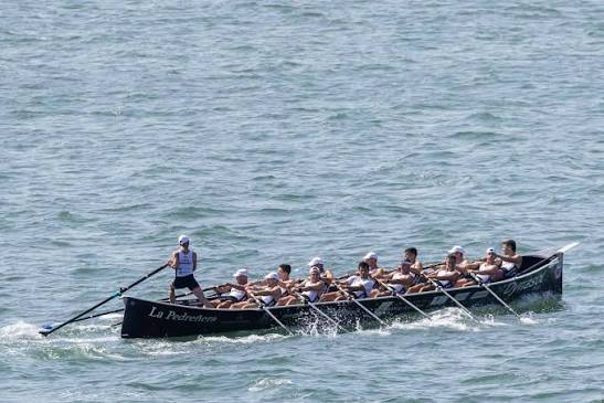 Trainera-Ruderboot bei einer Regatta der ARC1-Liga in der Bucht von Santander, mehrere Boote nebeneinander, sonniger Tag.