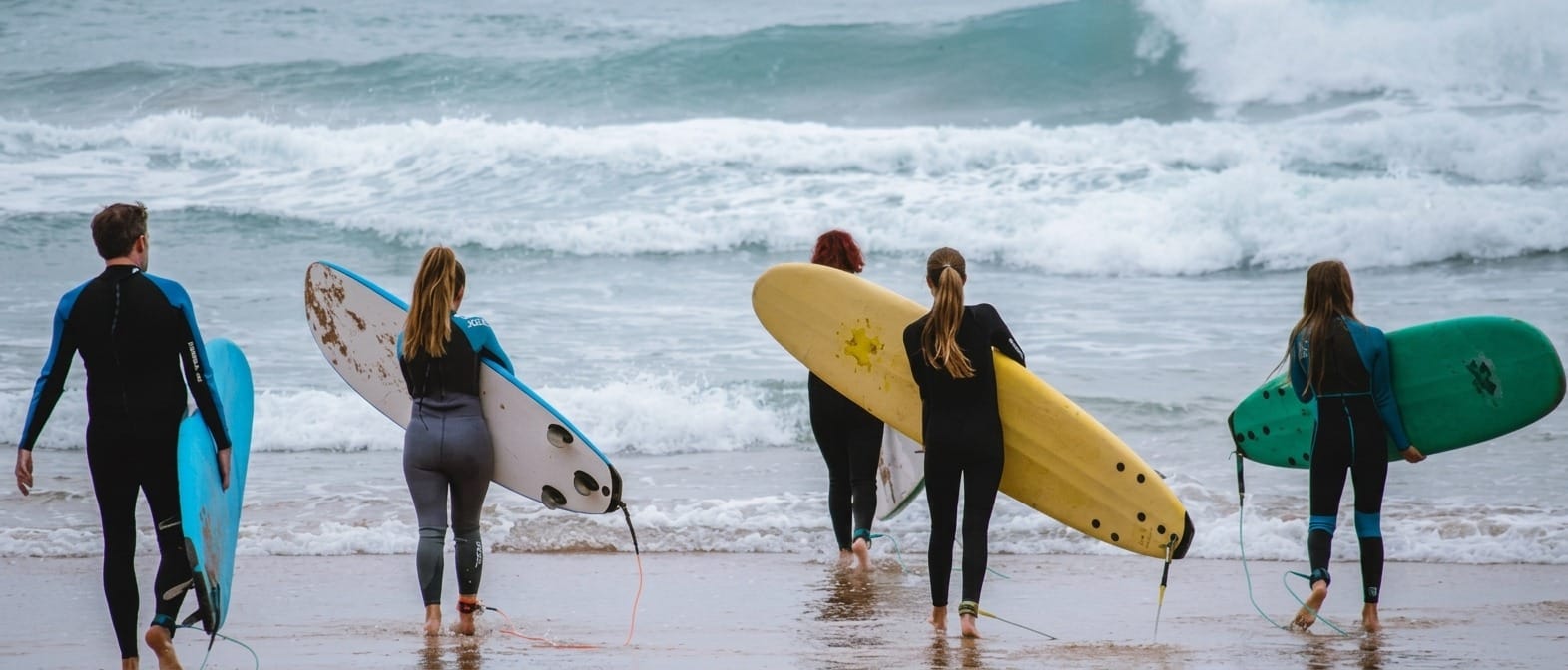 Grupo de principiantes con neopreno y tablas en la orilla de la playa de Ajo (Cuberris) con un monitor