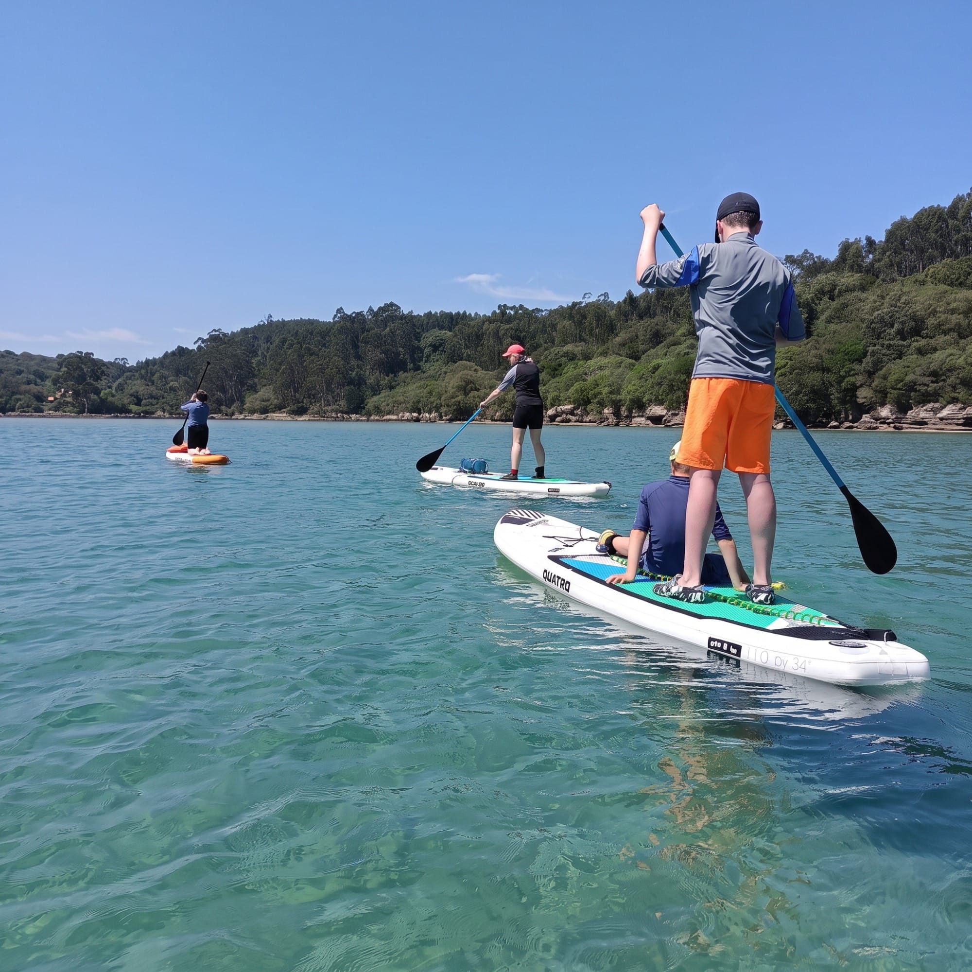 Grupo en paddle surf por las aguas planas de la ría de Ajo al fondo de la marisma