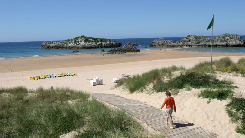 Übersicht über einen Strand bei Bareyo bei Ebbe mit leerem Flaggenmast an einem sonnigen Tag, ohne Badegäste im Vordergrund