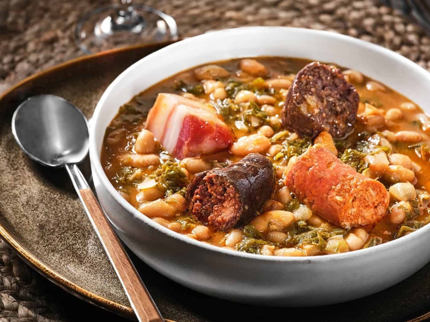 Dampfender Topf Cocido montañés auf einem Holztisch in einem rustikalen Restaurant