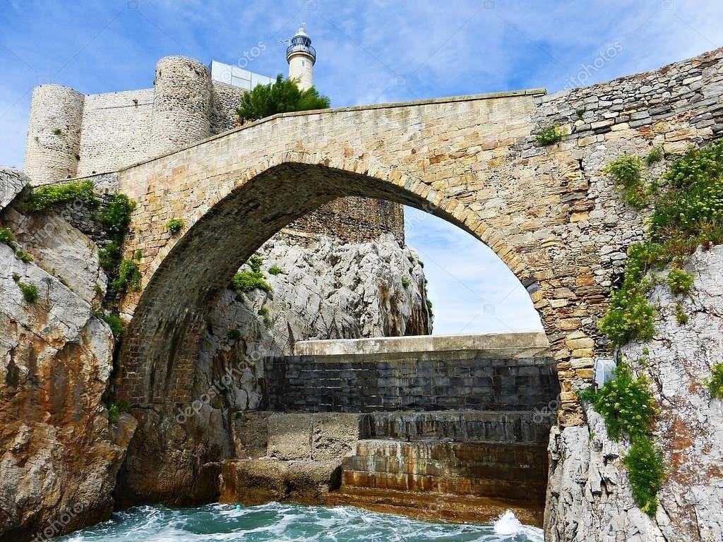 Puente medieval de un solo arco que lleva a la ermita de Santa Ana en Castro Urdiales, con el mar rompiendo alrededor