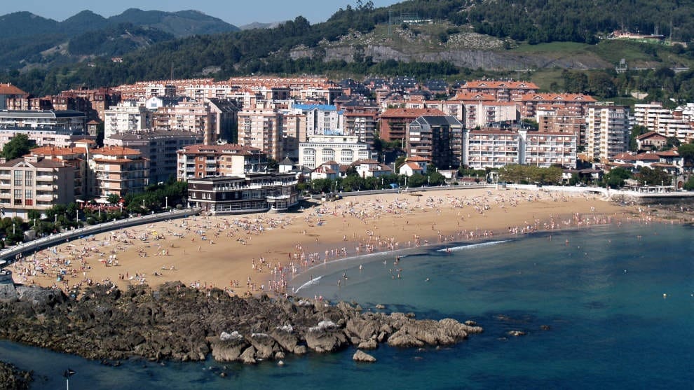 Playa de Brazomar en Castro Urdiales con el paseo marítimo, el dique de protección y bañistas en la arena