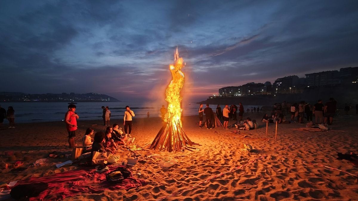 Hoguera de San Juan en una playa cántabra al anochecer, con gente alrededor