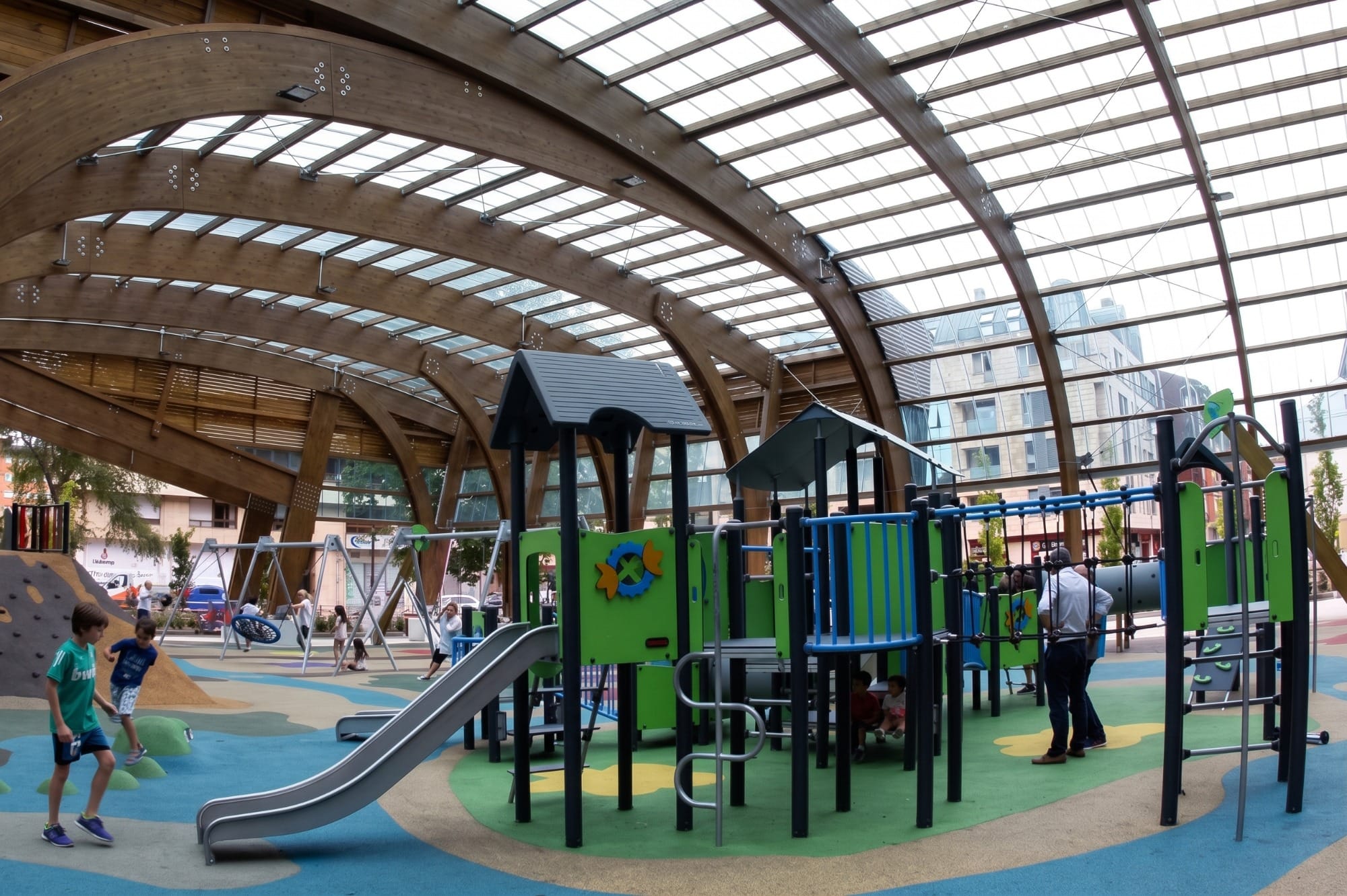 Niños jugando en un parque infantil cubierto en un día de lluvia, vista general del interior