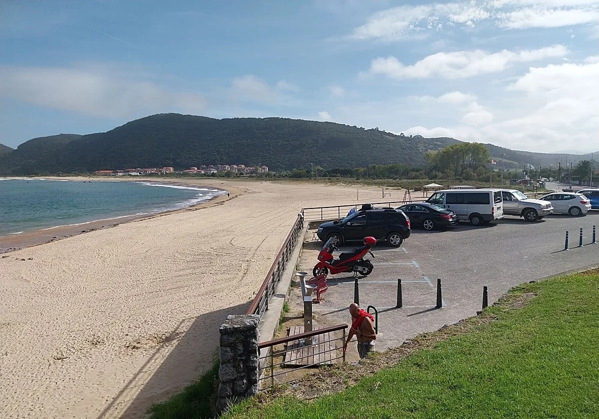 Rented sunbeds and umbrellas lined up on the sand of a Cantabrian beach, with promenade bars in the background