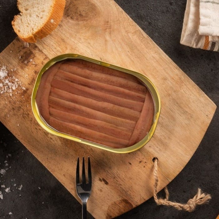 Conservas de anchoa de Santoña y pan sobre mesa de madera, luz natural