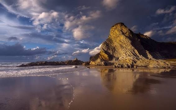 Cielo con nubes cargadas y claros sobre la costa cantábrica, mar en calma desde un acantilado