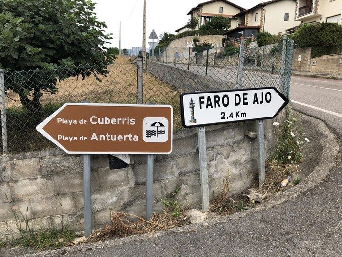Route rurale d'accès au quartier d'Ajo, à Bareyo, avec des champs verts et une signalisation locale de part et d'autre