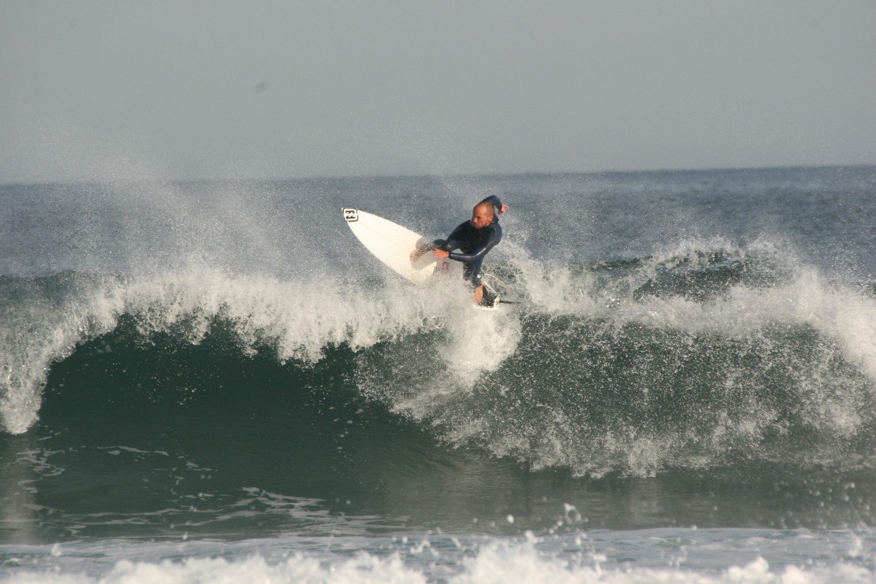 Surfers entering the water at Playa del Puntal with open Cantabrian Sea swell, autumn afternoon