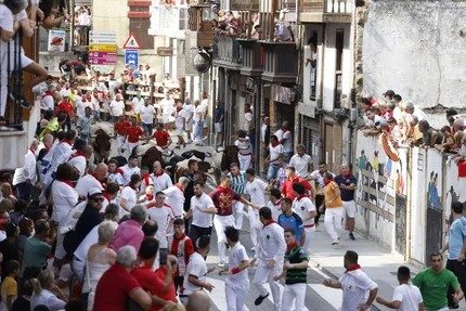 Läufer und Stiere überqueren die Puente Grande über die Calle José Antonio in Ampuero während eines der Mittags-Stierläufe.