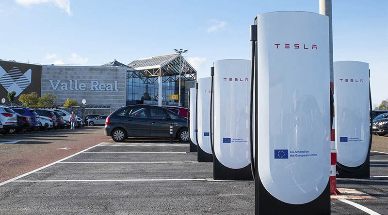 An electric car charging at a Tesla Supercharger point next to a shopping centre